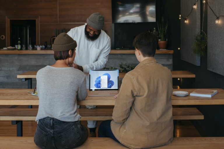 Three people sitting on benches at work around a Microsoft laptop